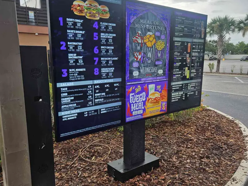 Freestanding three-panel digital drive-thru menu board live in a landscaped island